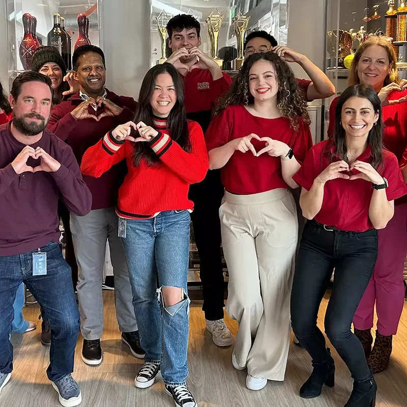 A group of Xactly employees all wearing red make heart shapes with their hands.