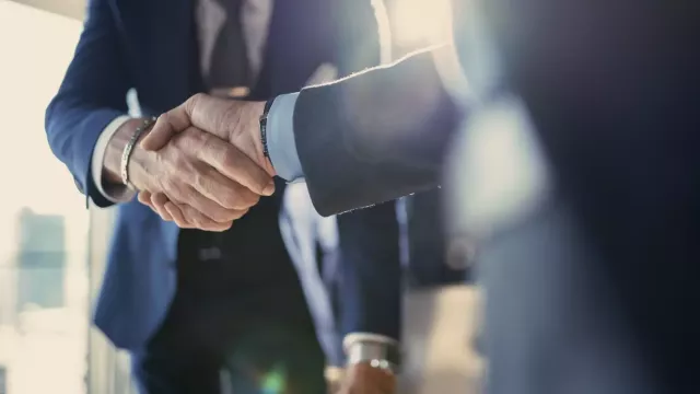 Two businessmen in suits shaking hands in a close of photo not showing their faces with lens flare.