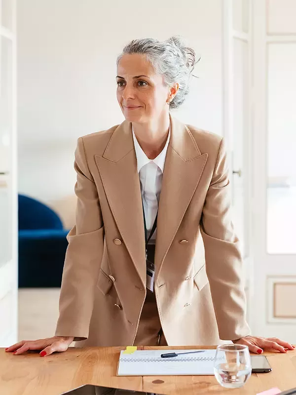 A stylish woman in a suit and tie exudes professionalism as she stands at the head of a conference table, commanding attention and respect.