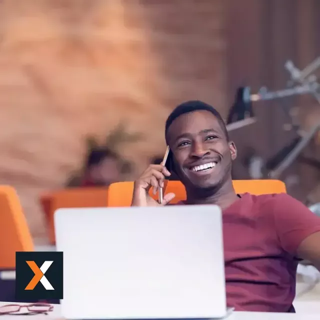 Man sitting at desk with laptop facing camera smiling while on the phone