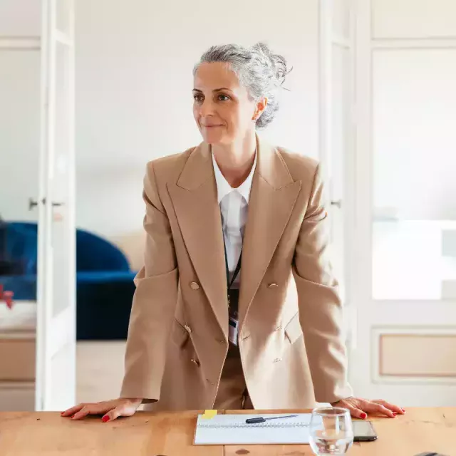 A businesswoman in formal attire standing by a desk.