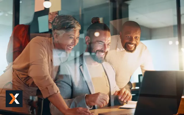 Group of coworkers sitting at table working and smiling off one laptop