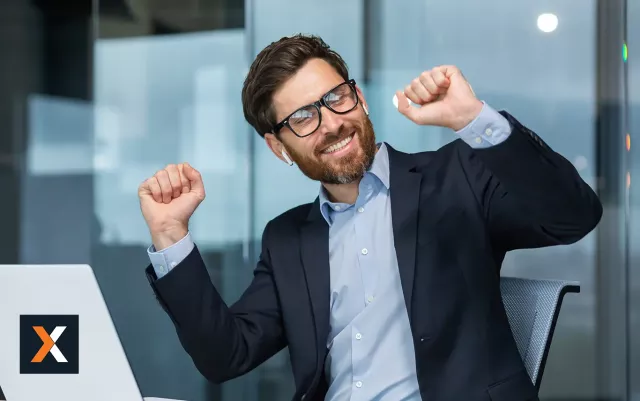 Businessman sitting at computer desk with headphones on cheering